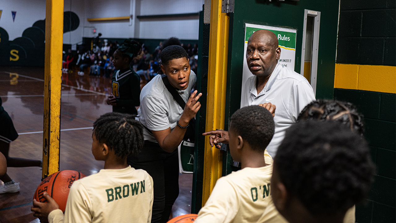 Young men holding basketballs standing inside door with older coach standing next to them
