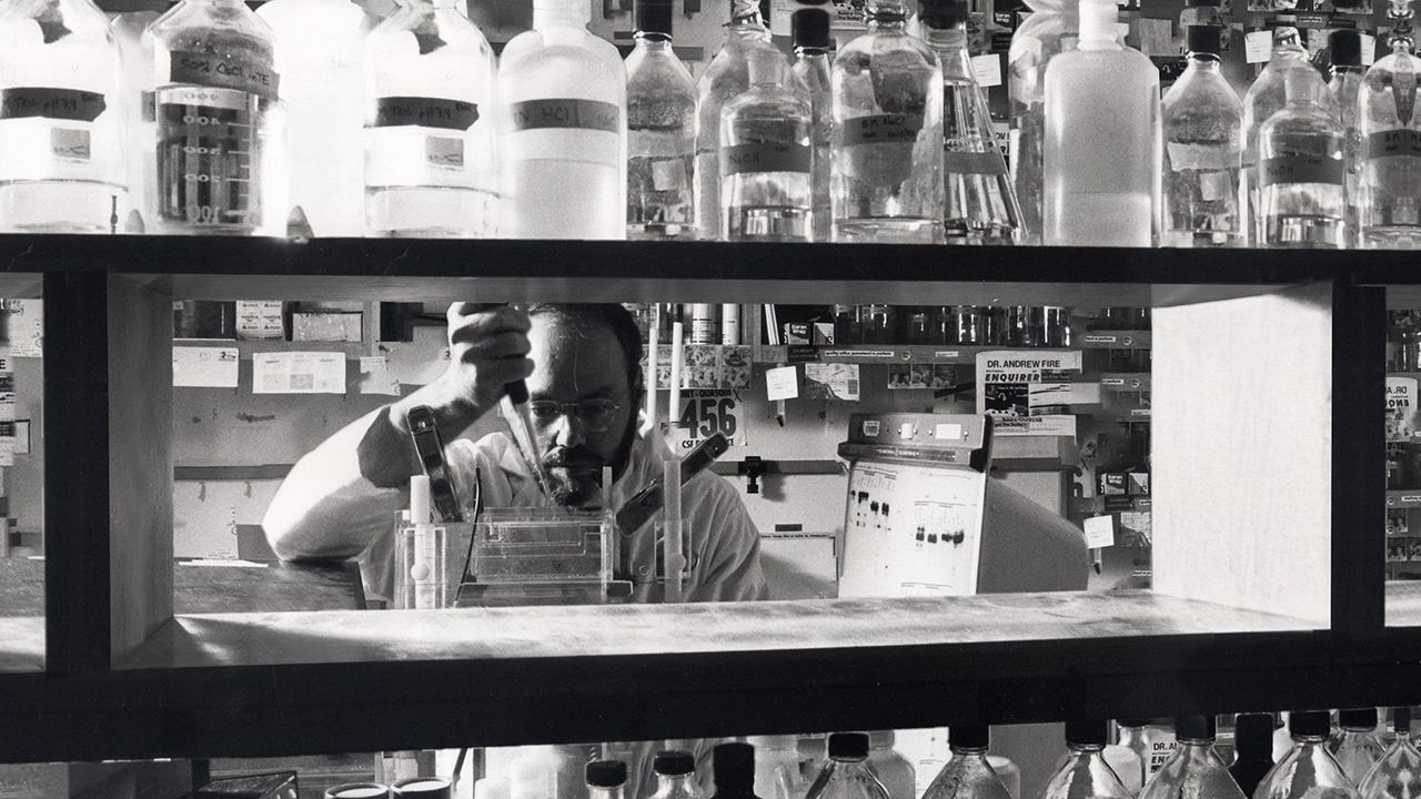 Man working in medical lab wearing a lab coat with light skintone and using a pipette