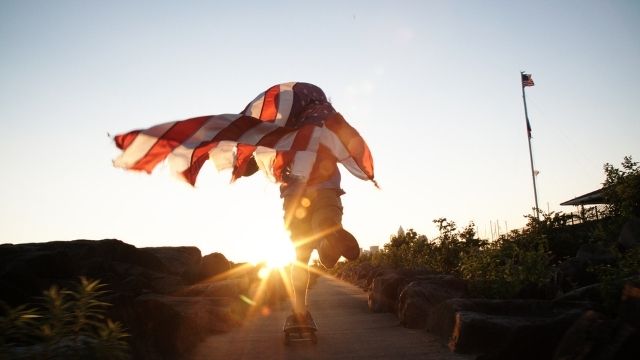 man running into the sunset with American flag wrapped around him