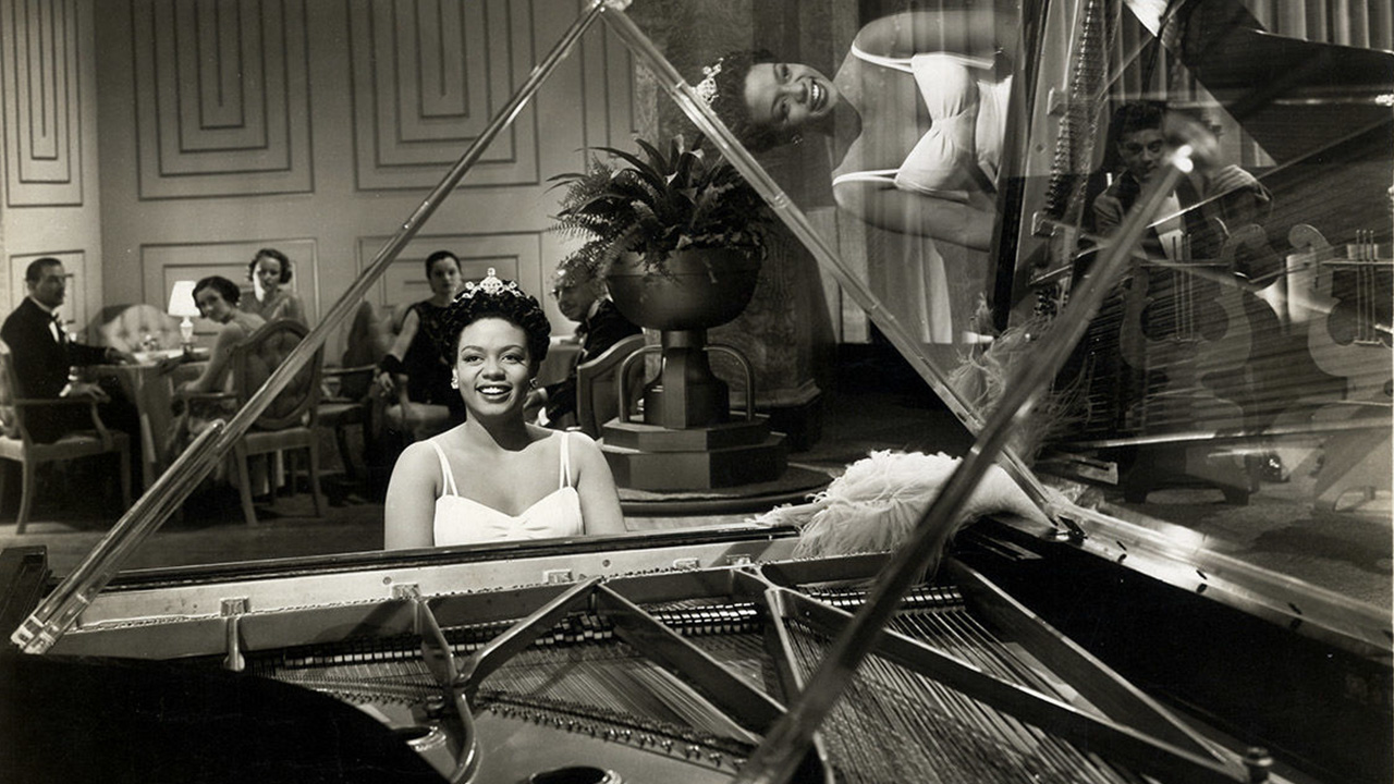 woman sitting at piano smiling playing for large room