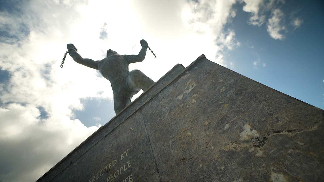 upward look at a statue framed in sunlight of man holding a chain