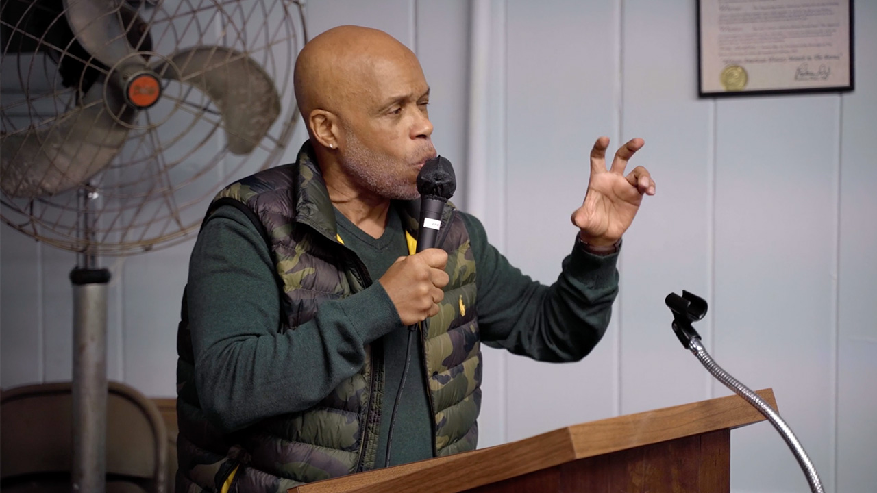 Man talking into microphone and gesturing with his hands