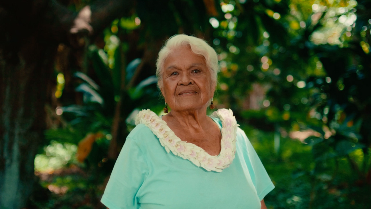 Older woman wearing a white Lei outside in a forest