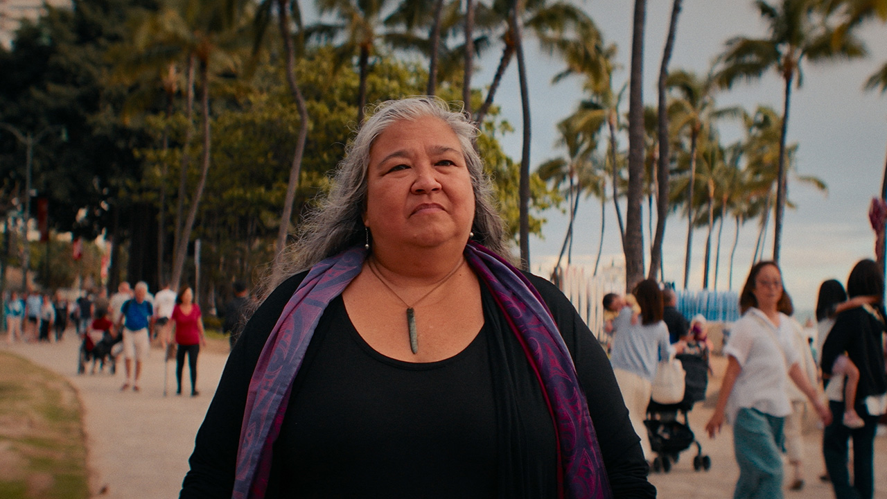 Native Hawaiian woman standing on a boardwalk that seems busy with tourists