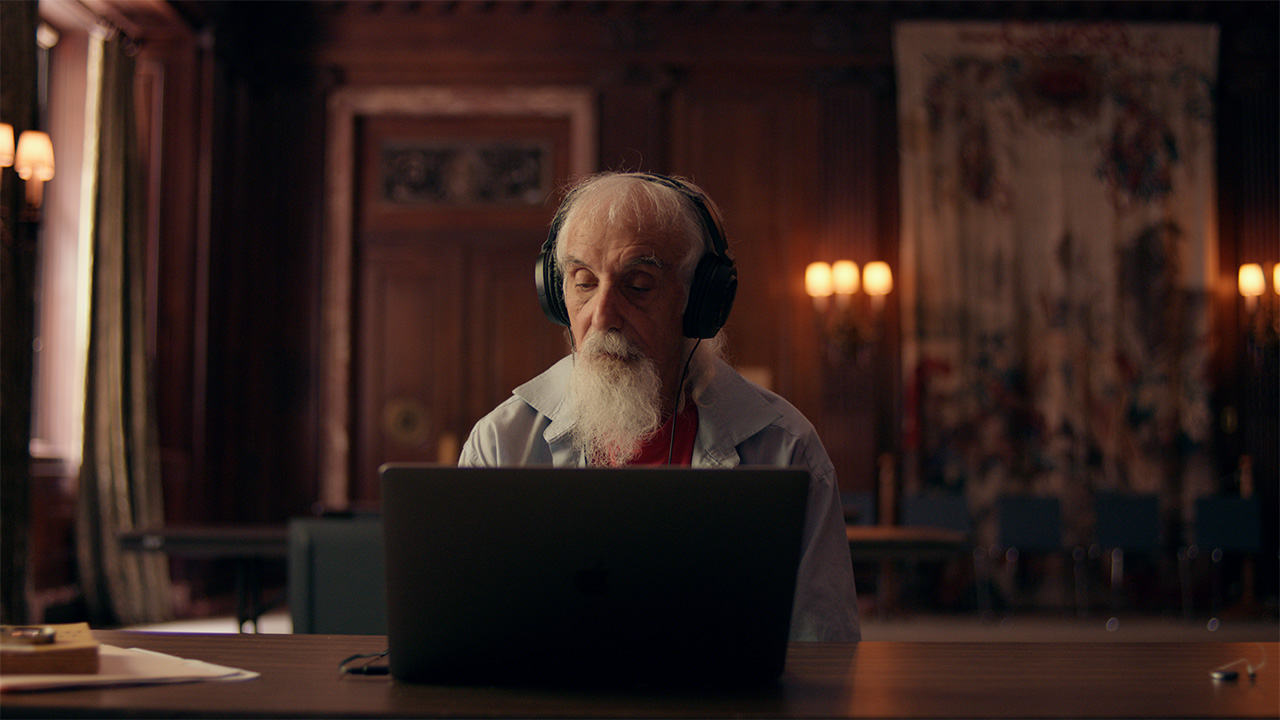 man with white hair wearing headphones looking at book