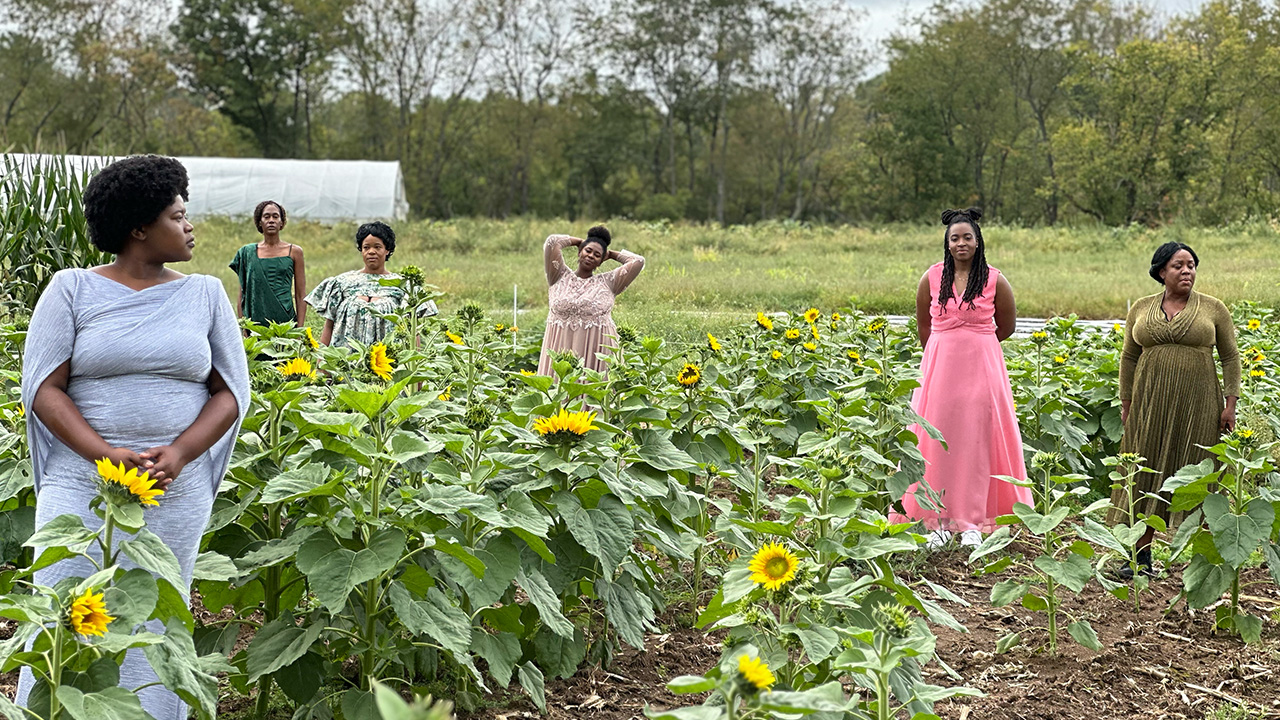 A group of women standing dispersed in a garden wearing nice clothes