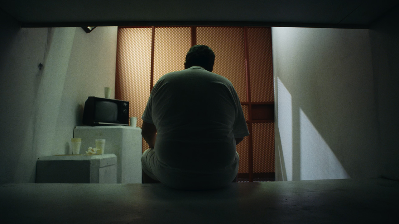 man with back to viewer sitting on bunkbed in prison cell