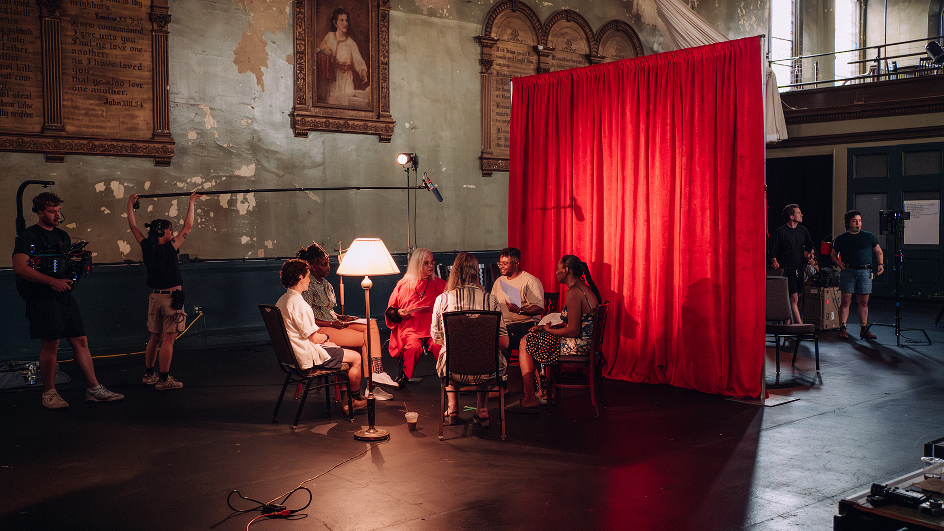 group of people sitting in a circle talking to each other with camera person and someone holding a mic. Shooting the discussion.
