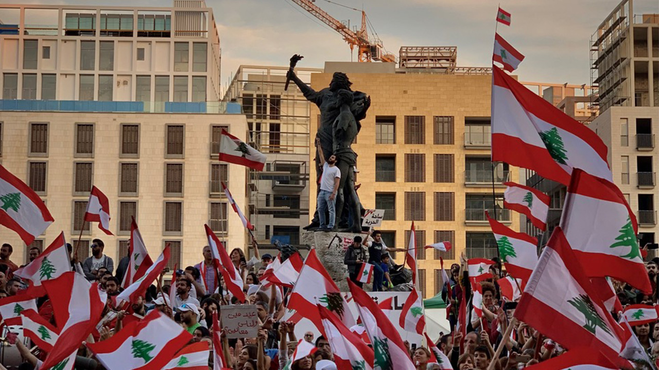 Man standing on statue in a crowd of people waving flags