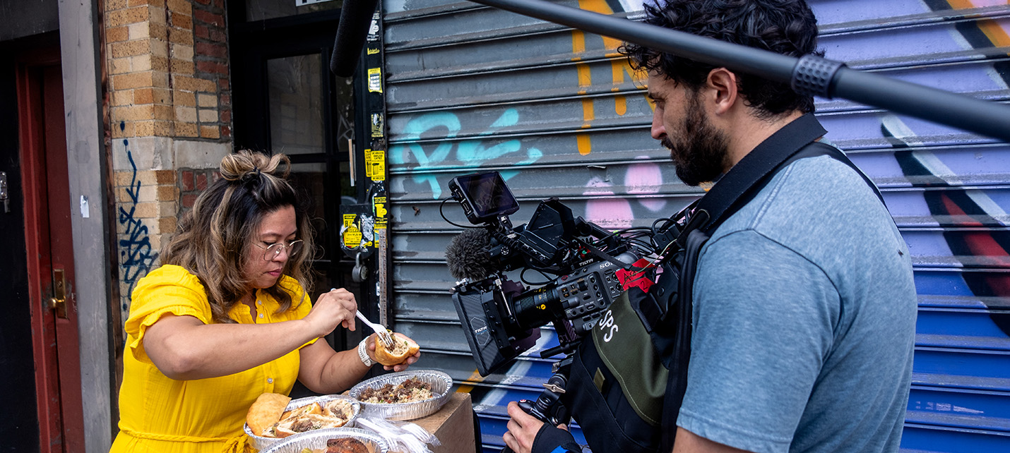 Chrissy Camba making a bite of food from trays on the street of new york with camera crew recording 